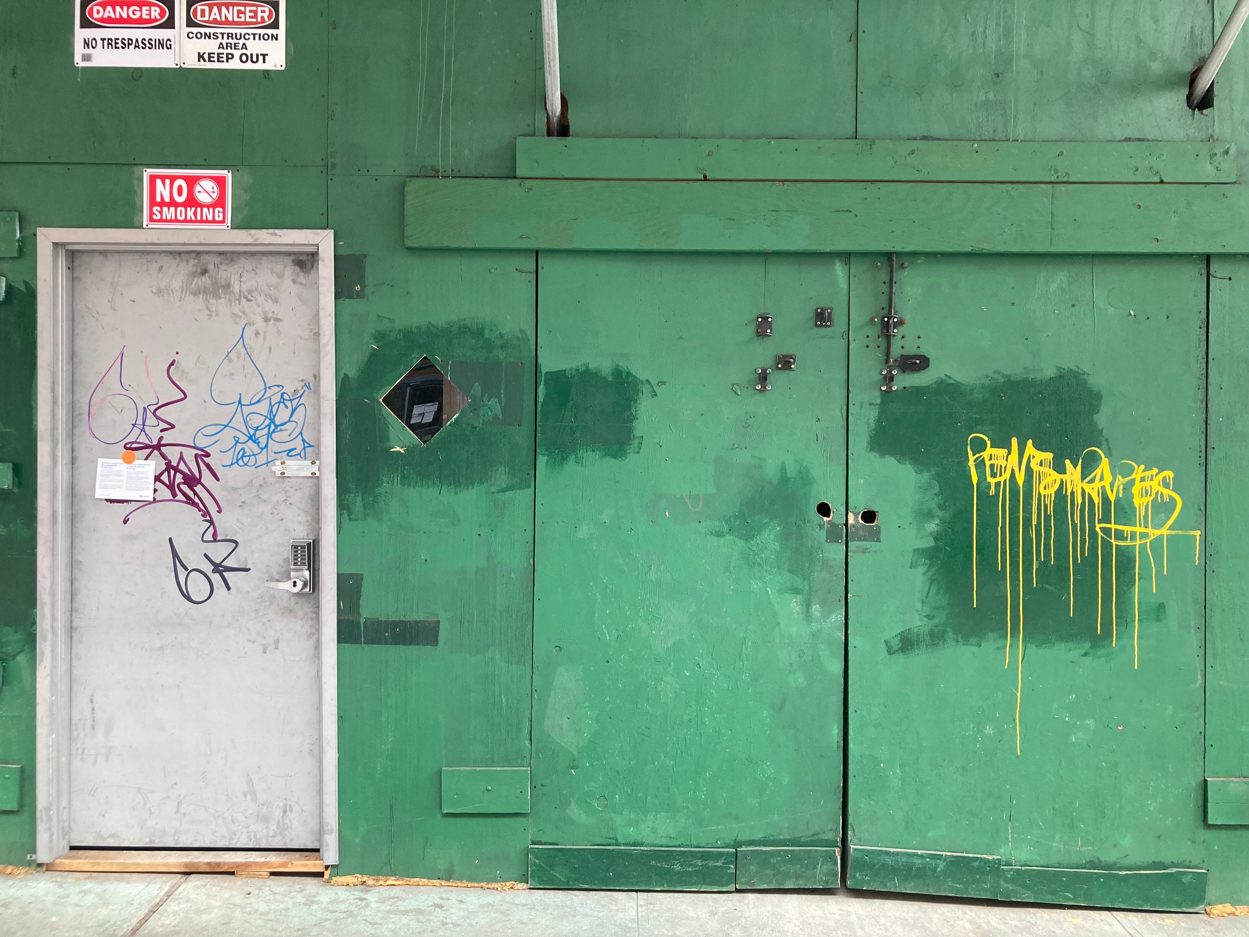 a green plywood wall with a metal door and green doors and several danger signs