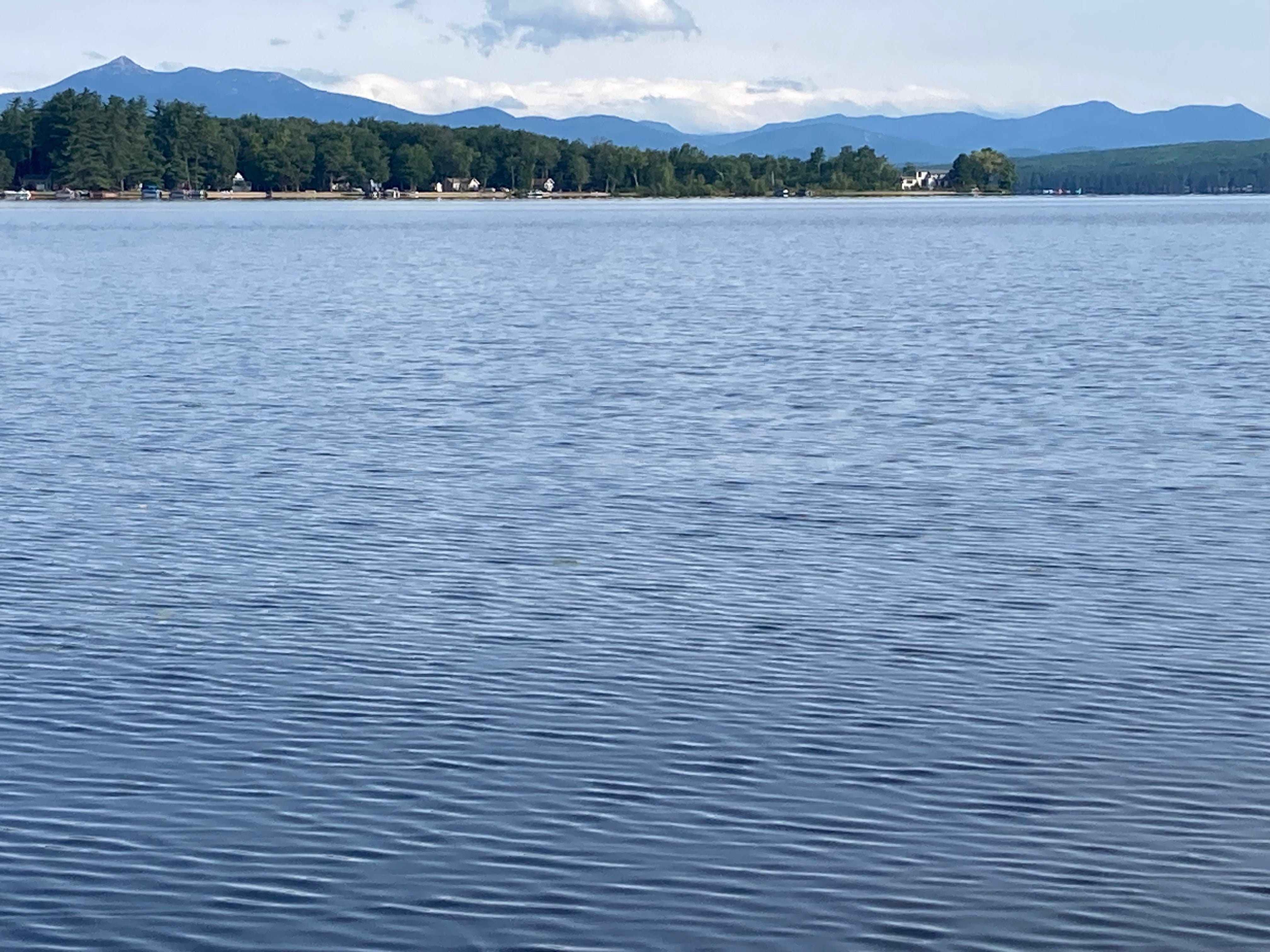 a view of a very blue lake with a rippled surface and mountains along the horizon beyond the other side of the lake