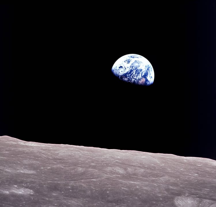 The lunar landscape is silvery gray and uneven, the sky is completely black, and a gibbous Earth glows blue and white.